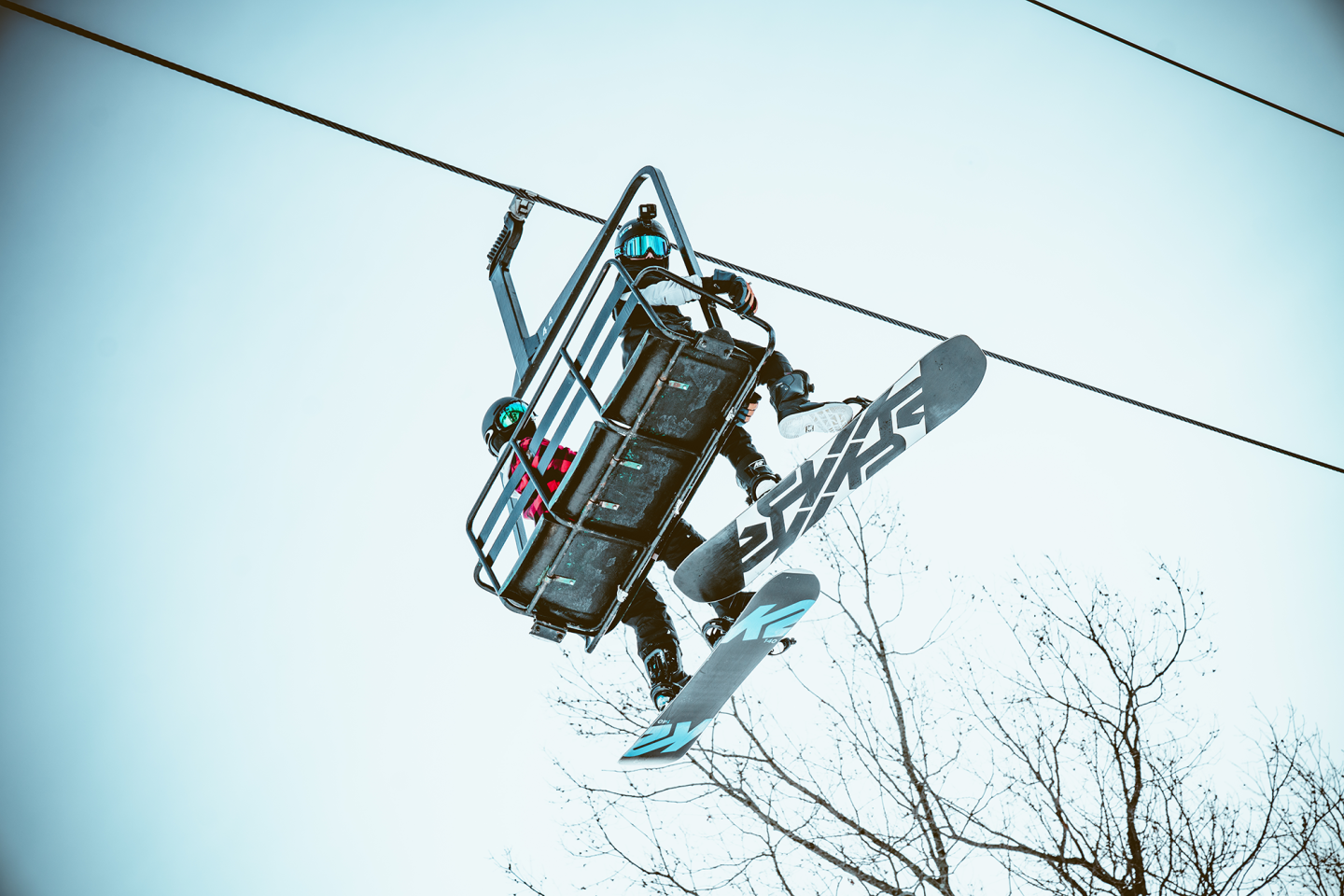 two snowboarders on chairlift, looking down at camera