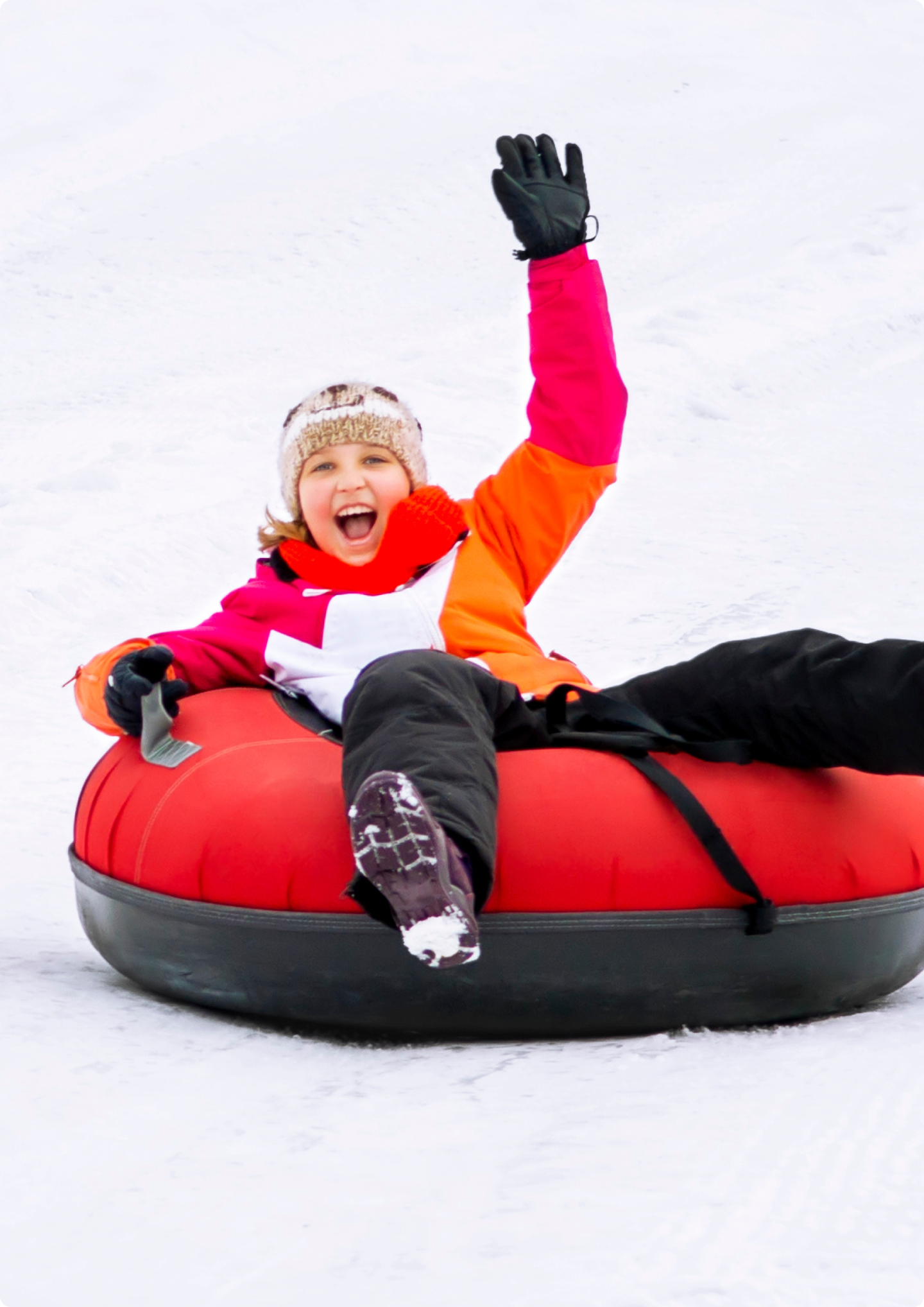Kid smiling with arm raised, while riding on snow tube