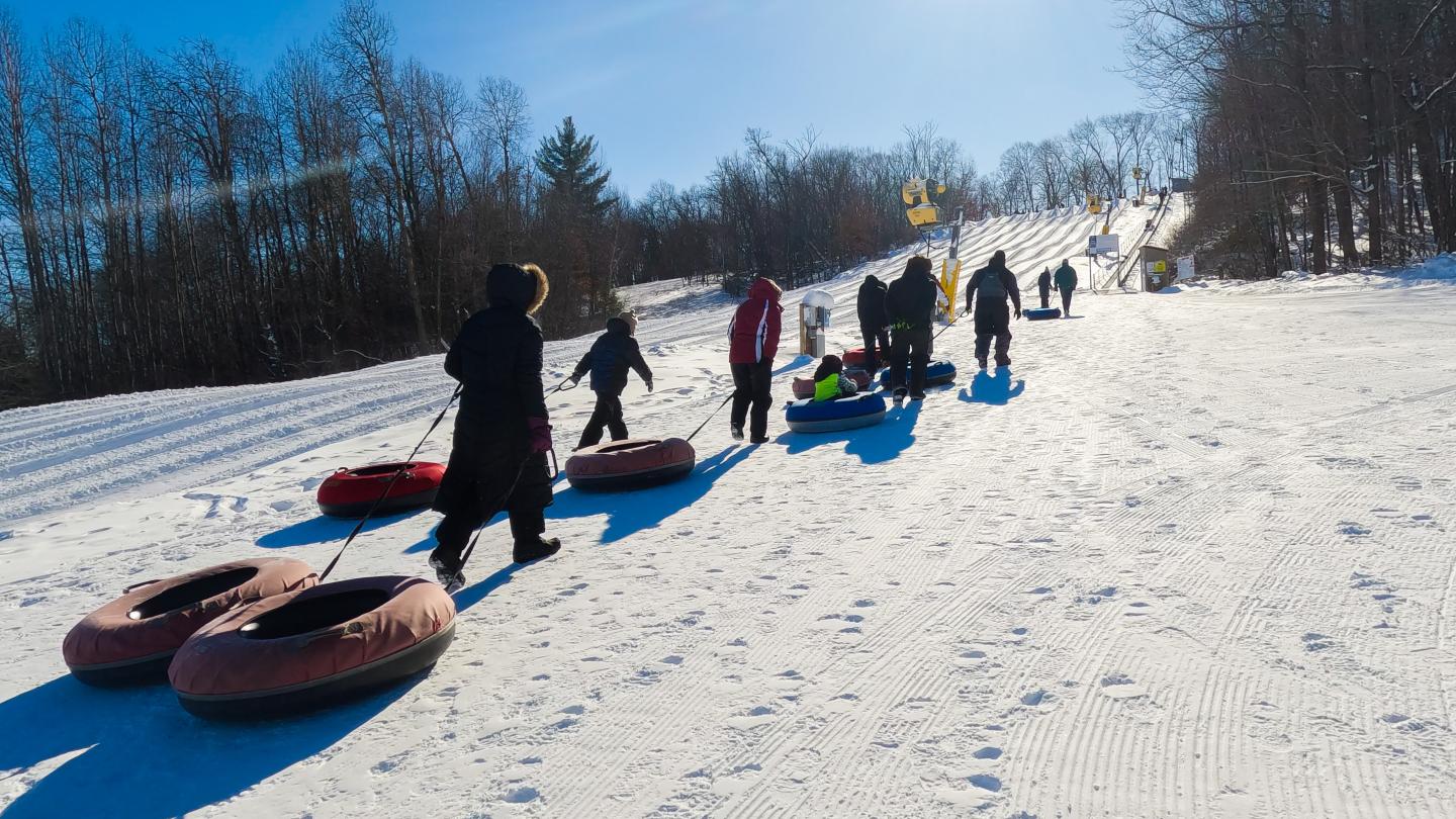 group of people pulling snow tubes up hill