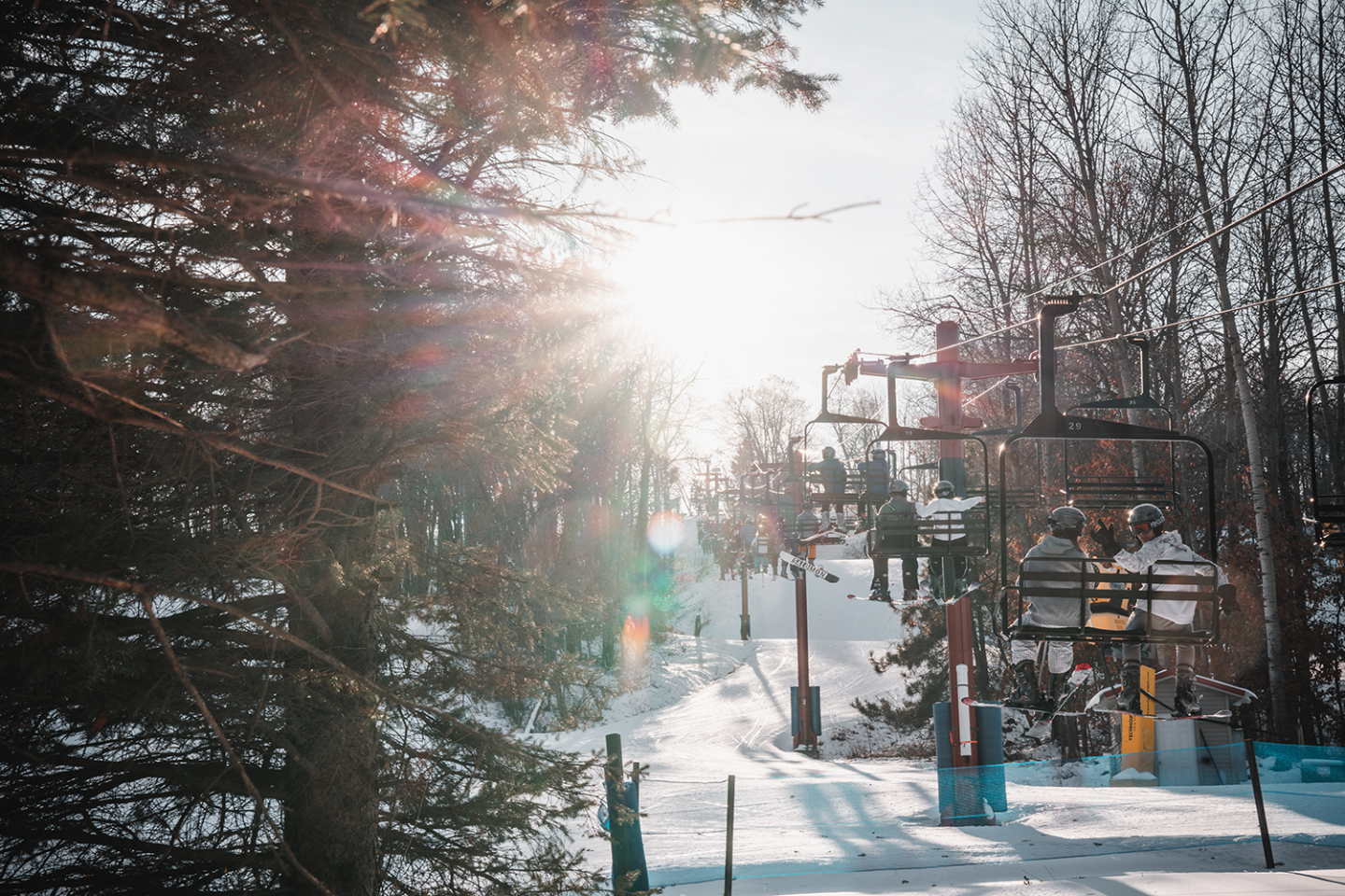People riding chairlift with trees in foreground