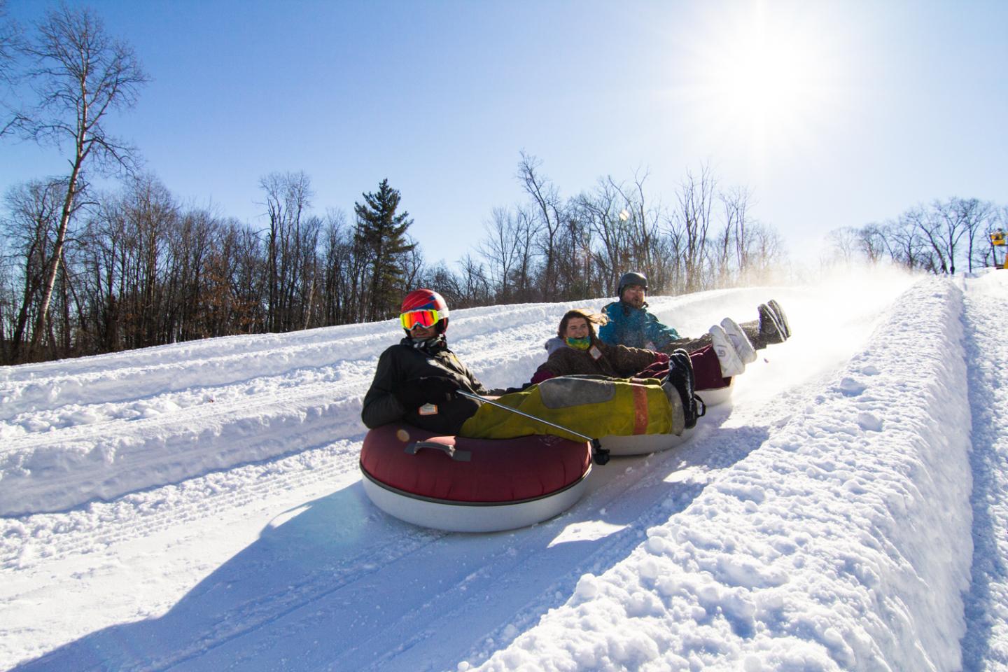 three people going down snow tubing track