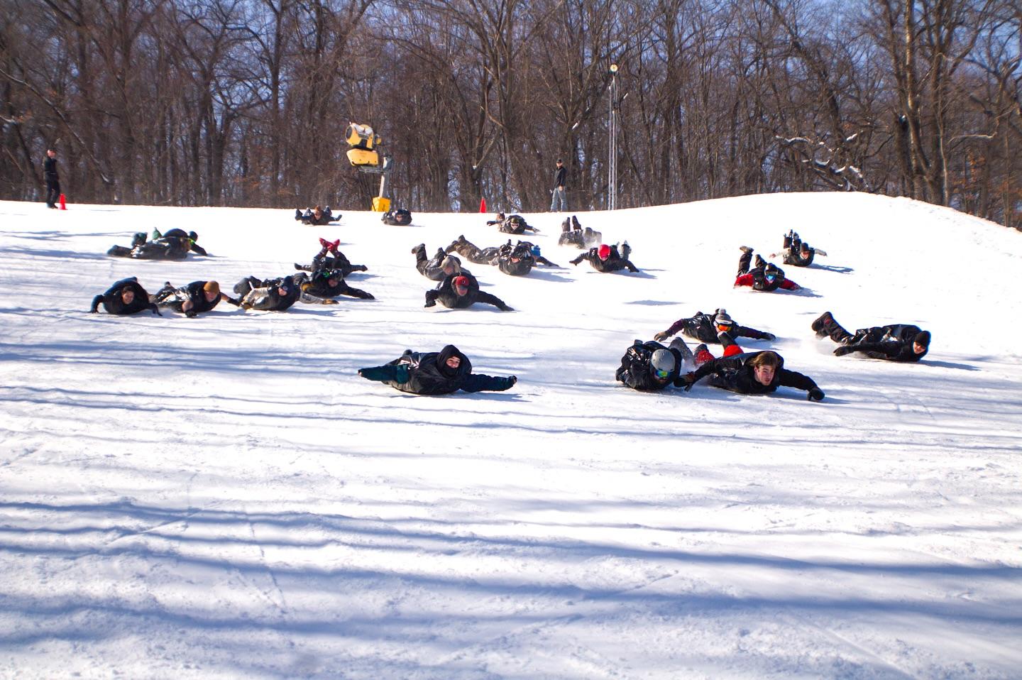 People tubing down snowy hill, scattered across slope, trees in background.