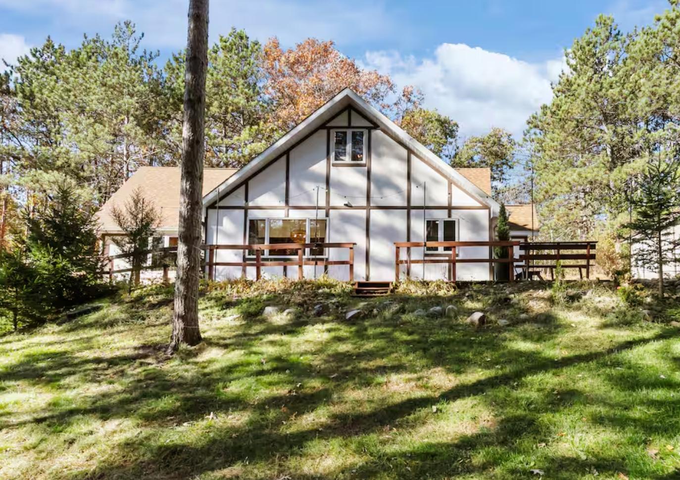 A-frame house with a wooden deck surrounded by trees under a blue sky.