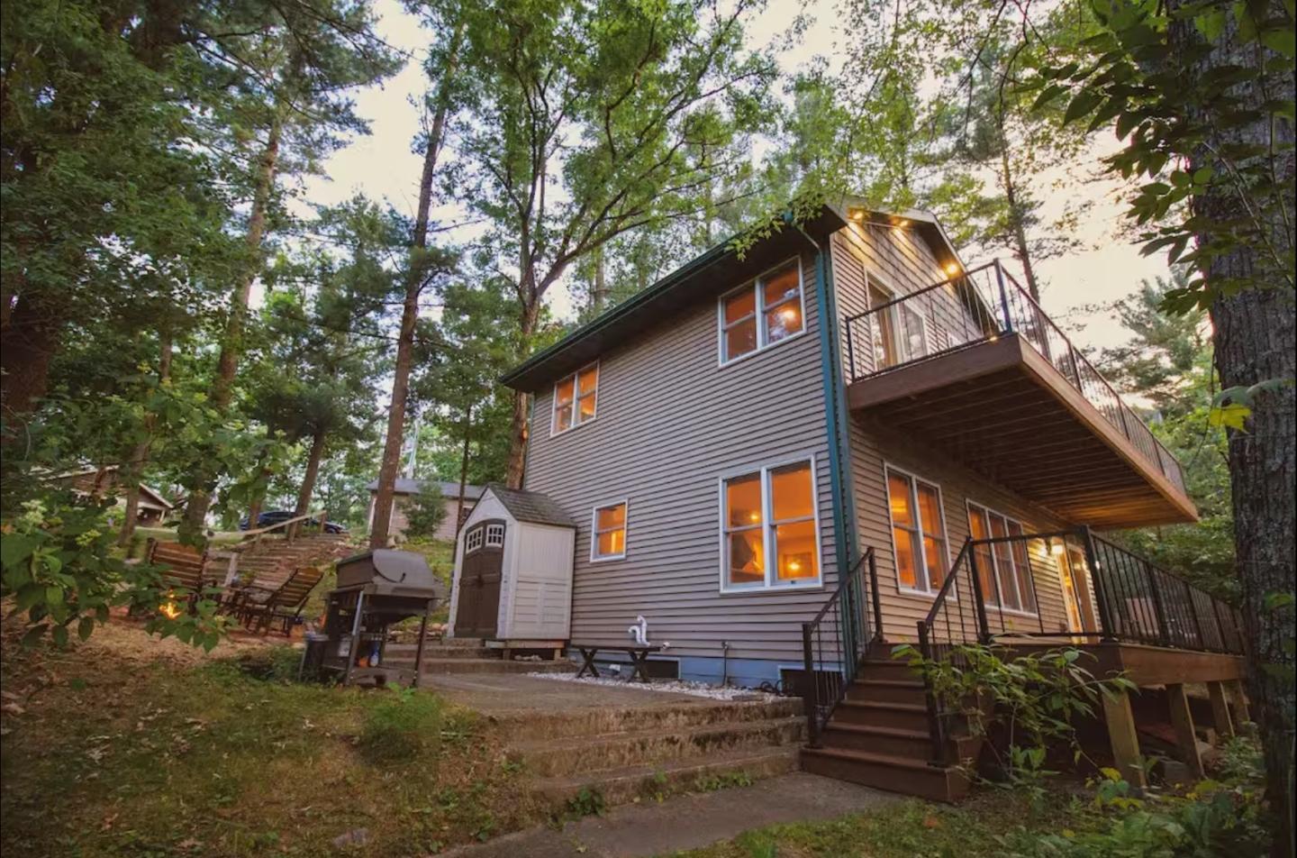 Cozy two-story house with lit windows, surrounded by trees.