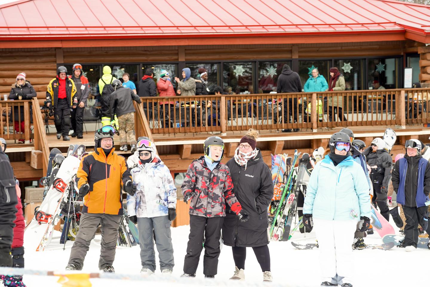 Group of skiers in colorful gear outside a log cabin.