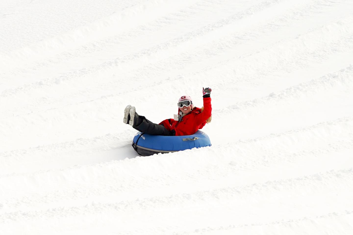 Person tubing down a snowy slope, wearing a red jacket and helmet.