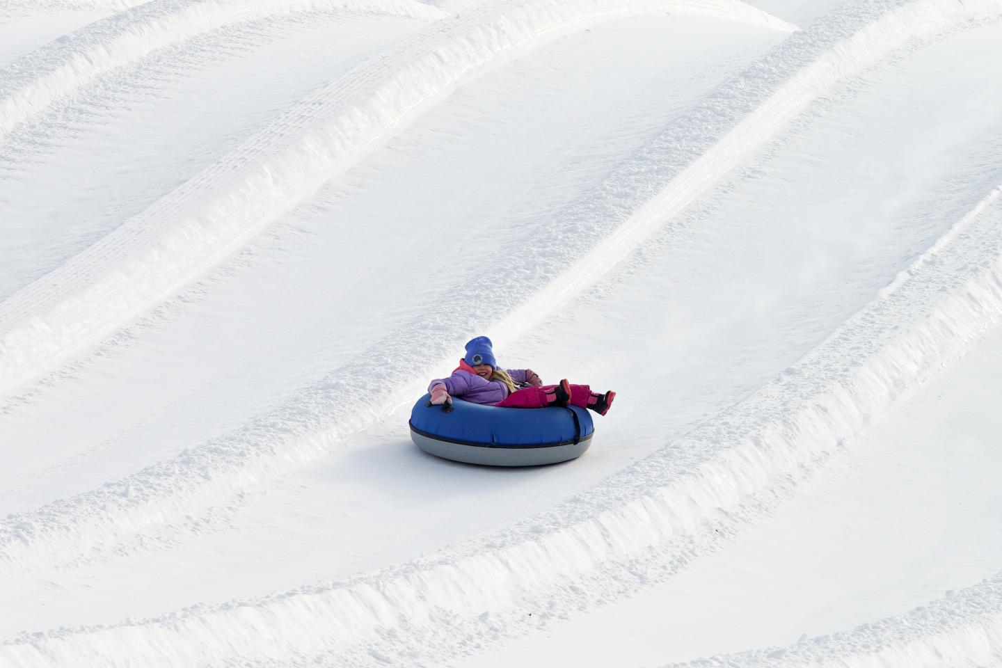 Person sledding down snowy hill on a blue inflatable tube.