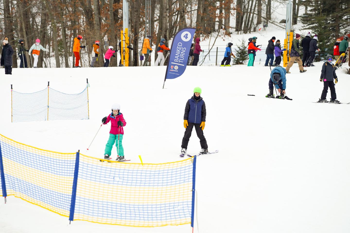 Skiers on a snowy slope with orange and yellow gate markers.