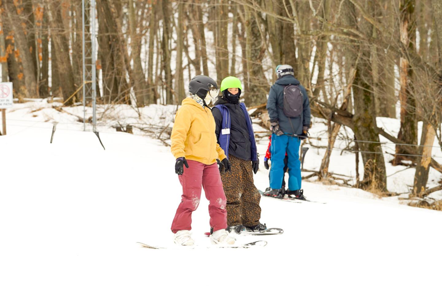 Three people skiing on a snowy trail with trees in the background.
