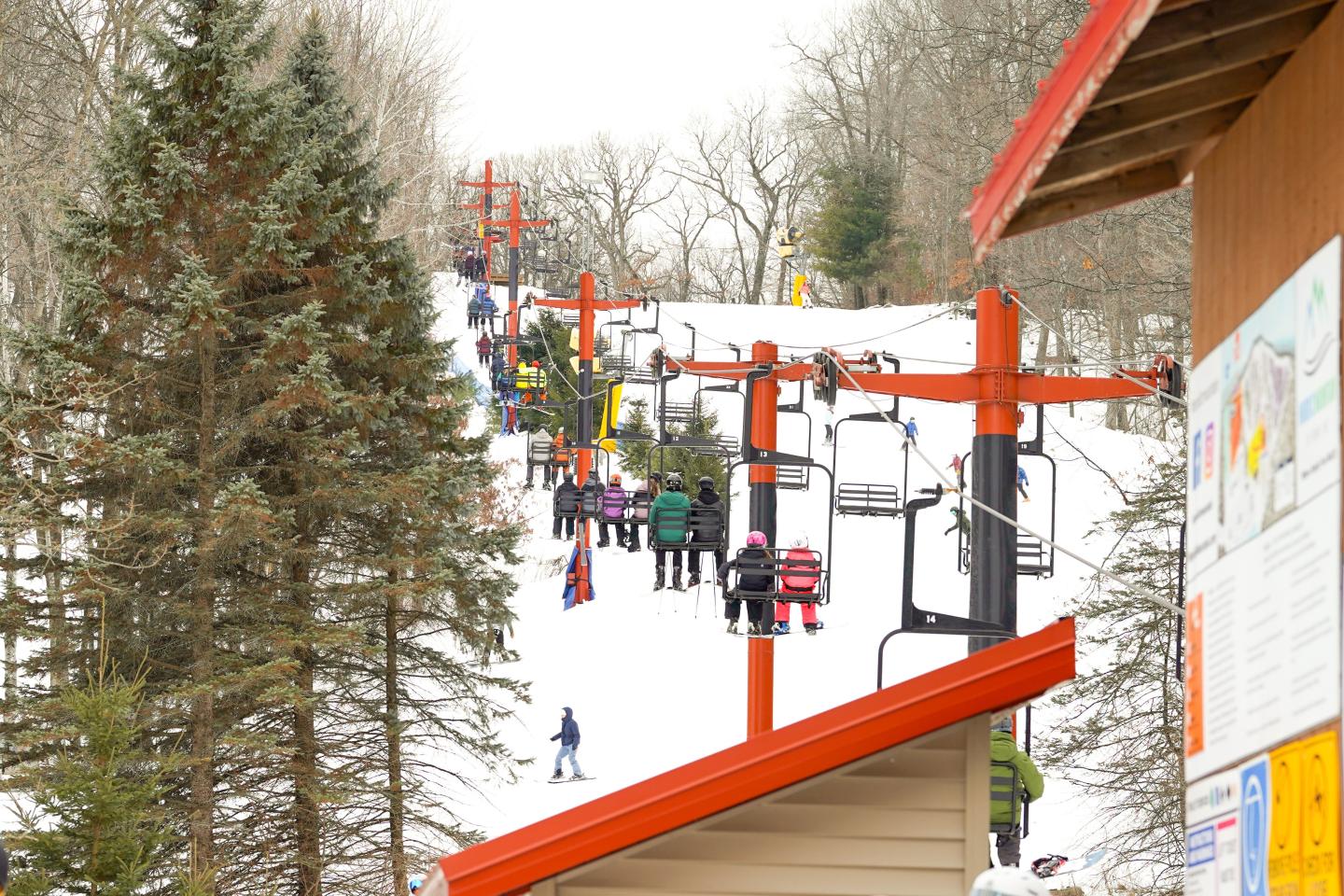 Ski lift ascending snowy hillside, surrounded by trees.