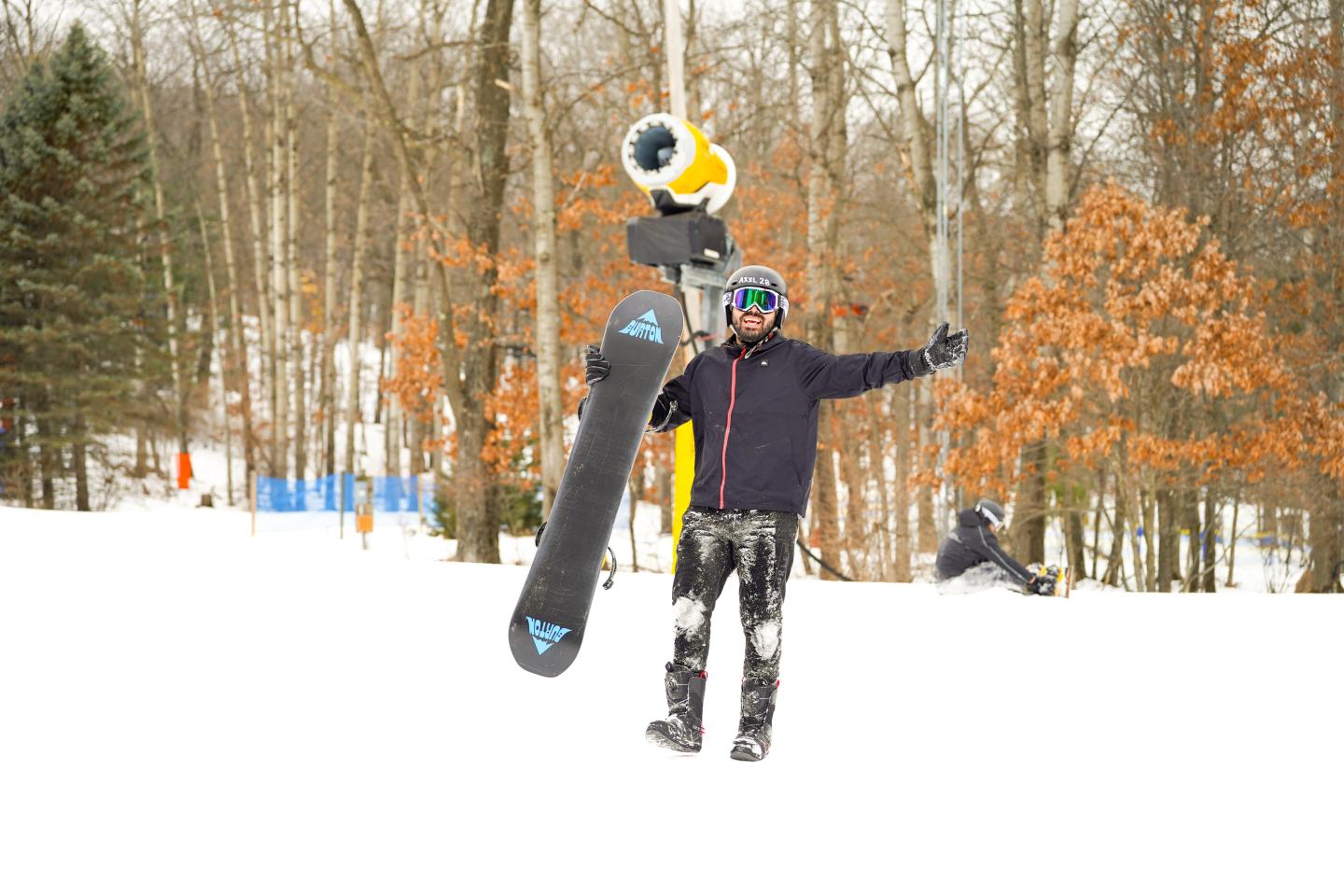 Snowboarder posing with arms outstretched on a snowy slope, surrounded by trees.