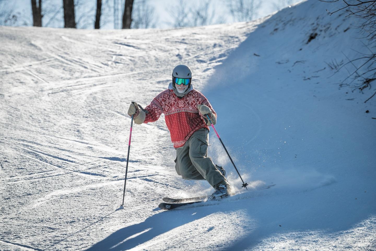 Skier in red jacket and helmet glides down snowy slope on a sunny day.