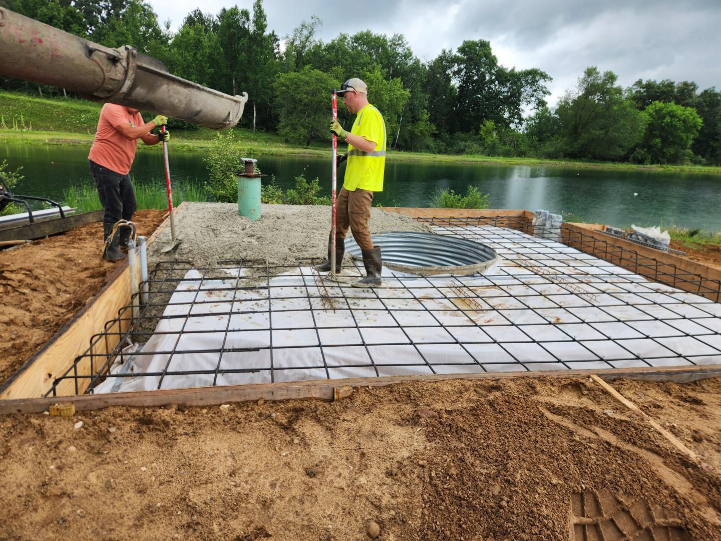 Two workers prepare rebar for a concrete slab beside a lake.