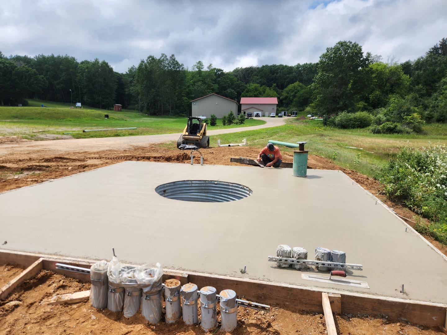 Freshly poured concrete slab at a rural construction site, with workers and equipment.