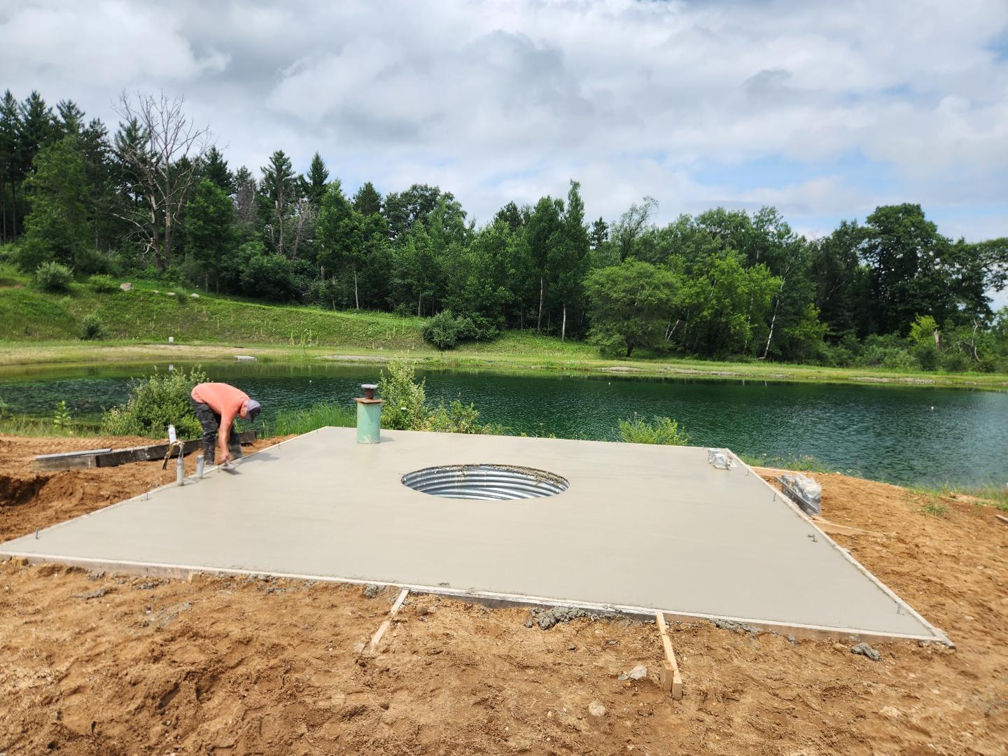 Freshly poured concrete slab beside a pond, with workers in the background.