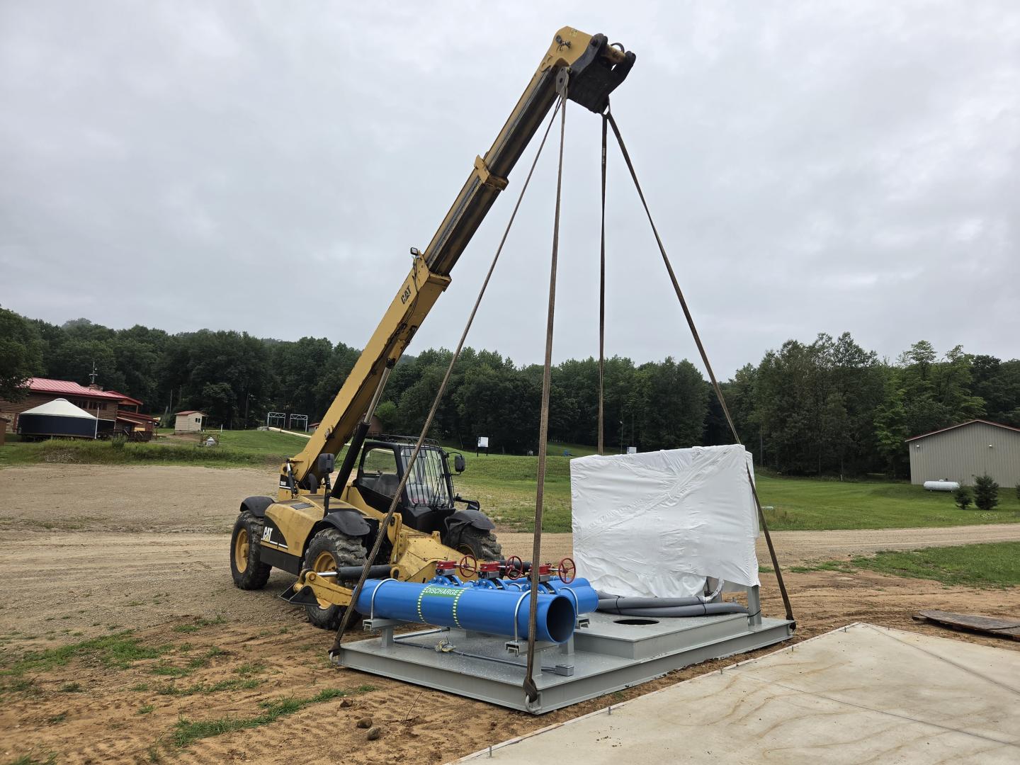 Mobile crane lifting a wrapped white load beside blue pipes at a construction site.