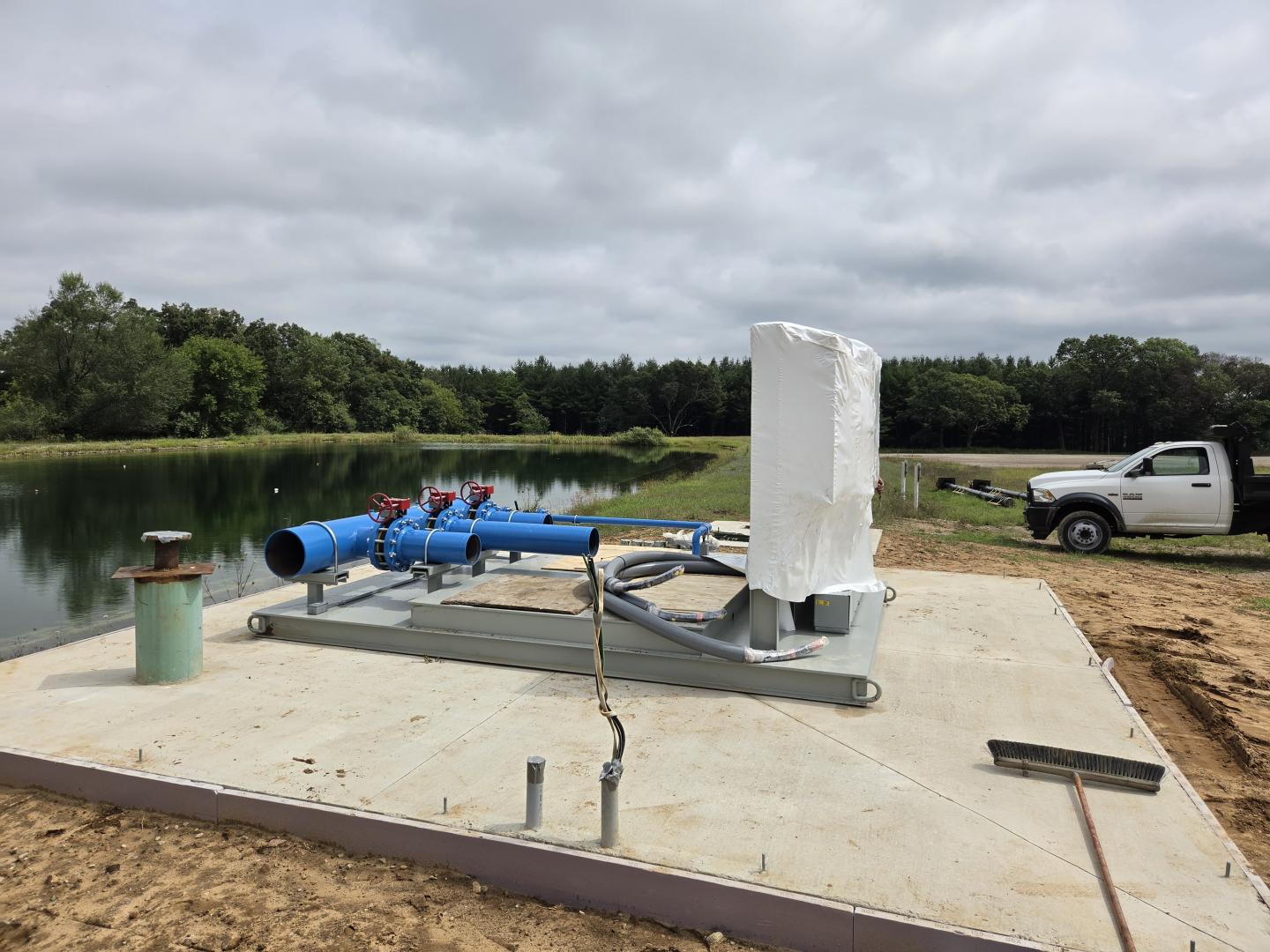 Concrete foundation slab with plumbing, construction materials, and a white wrapped column.
