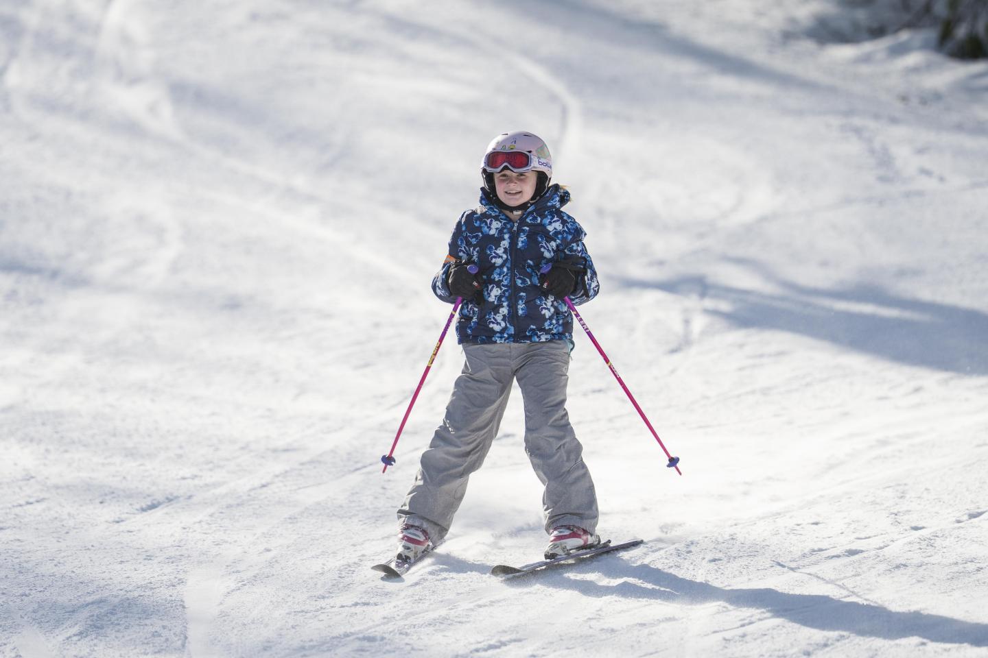 Child skiing downhill on a snowy slope with pink ski poles.