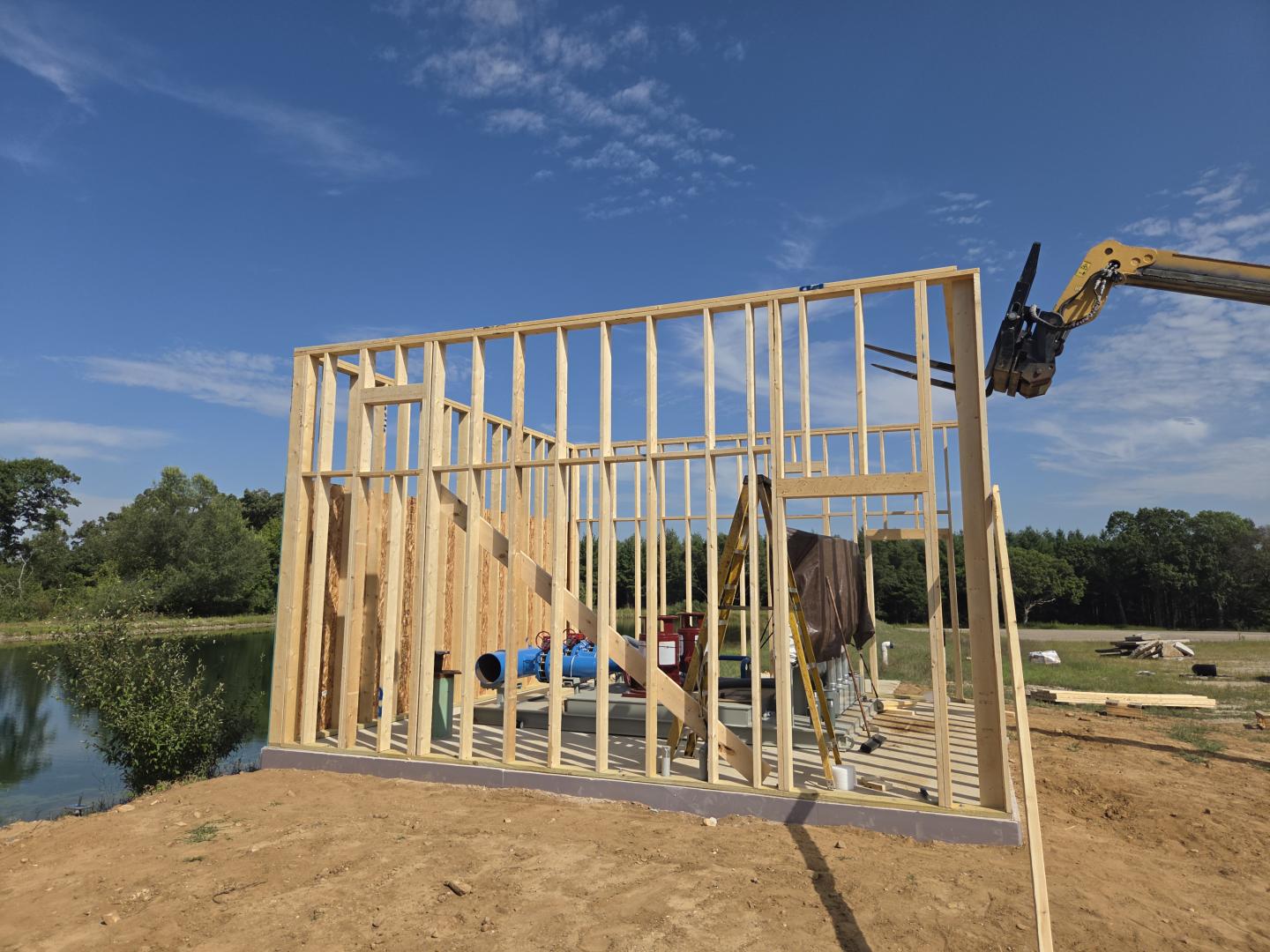 Workers framing a wooden wall at a construction site beside a pond.