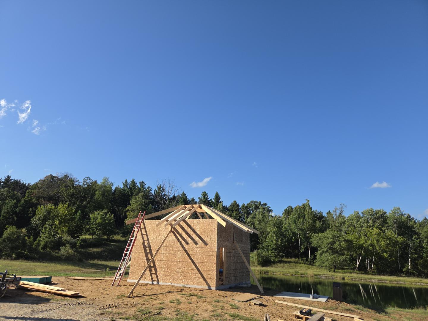 Wooden house frame under construction in a grassy rural field.