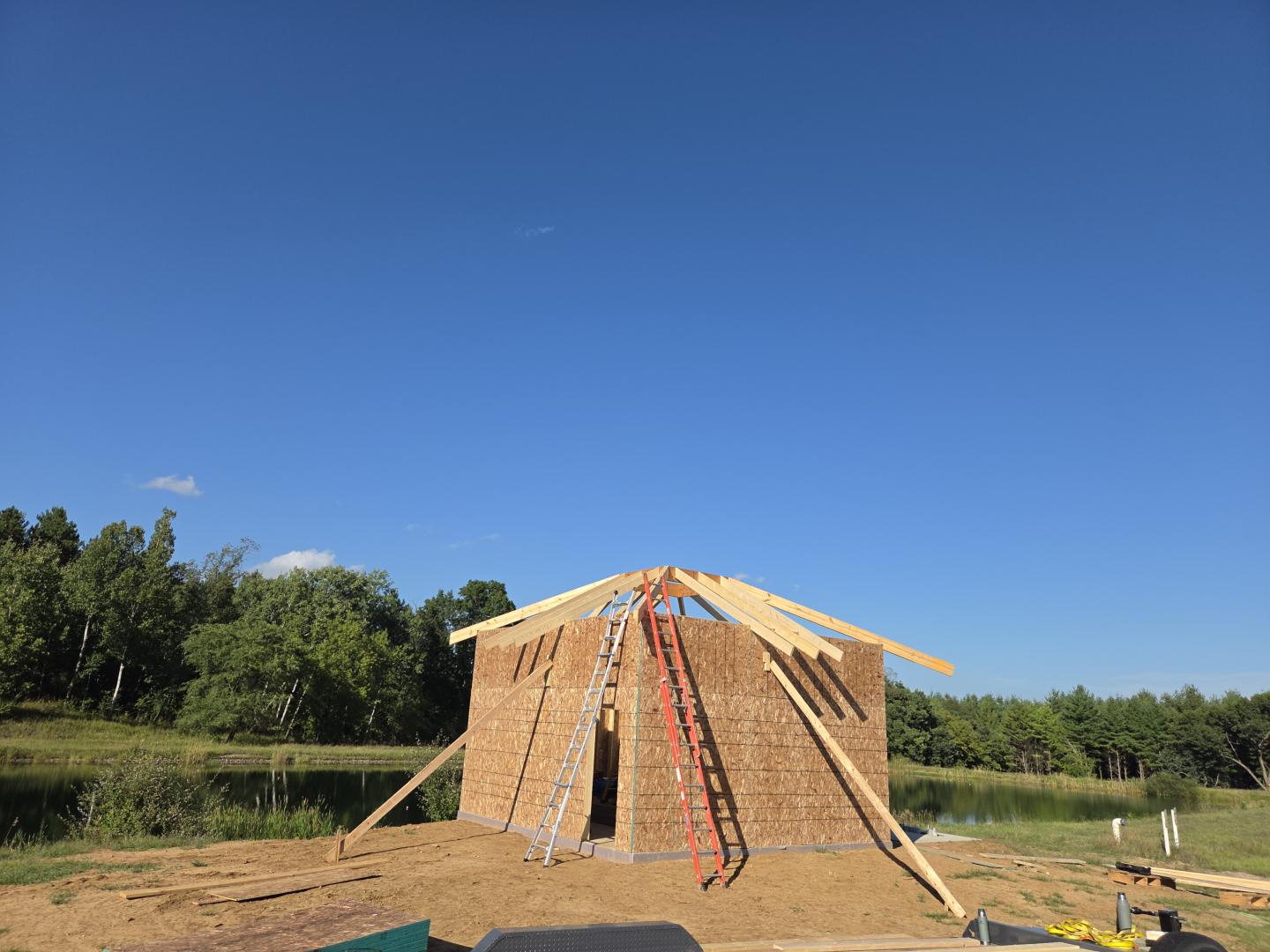 Wooden house frame under construction beneath a clear blue sky.