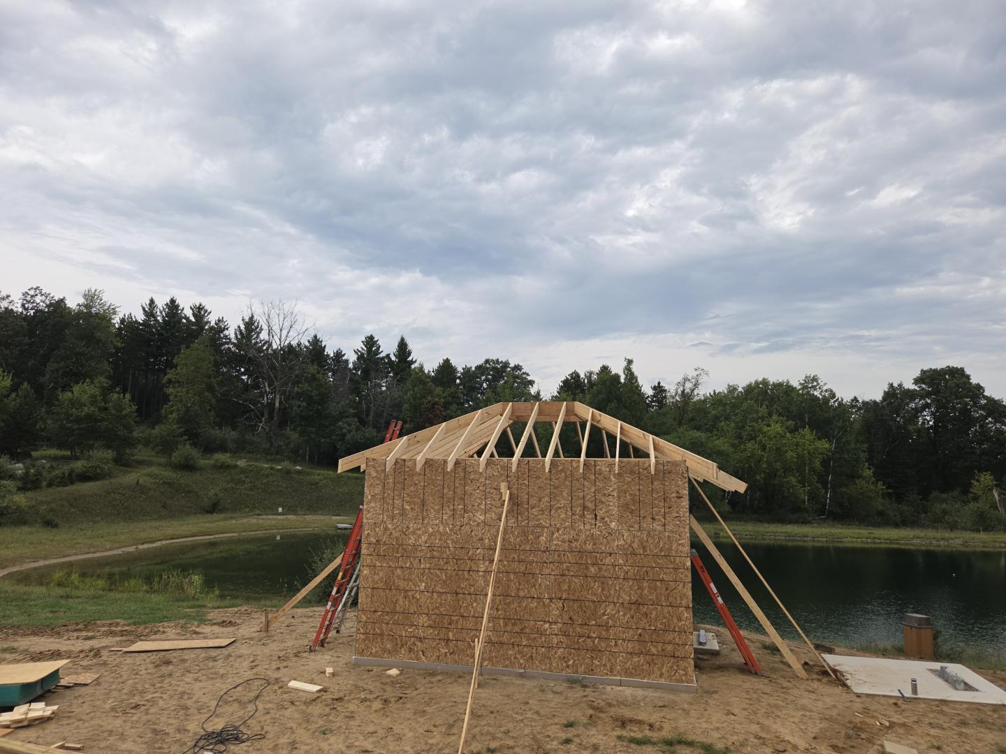 Wooden arched bridge under construction beside a lake.