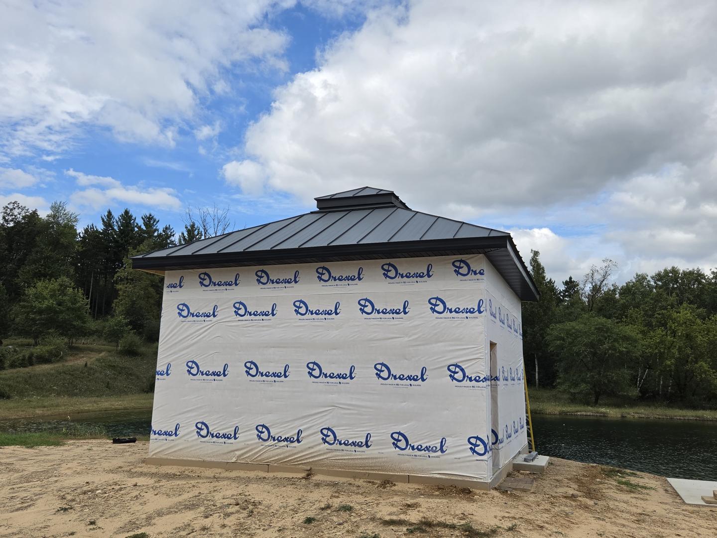Small white house wrapped in branded construction material beside a pond.