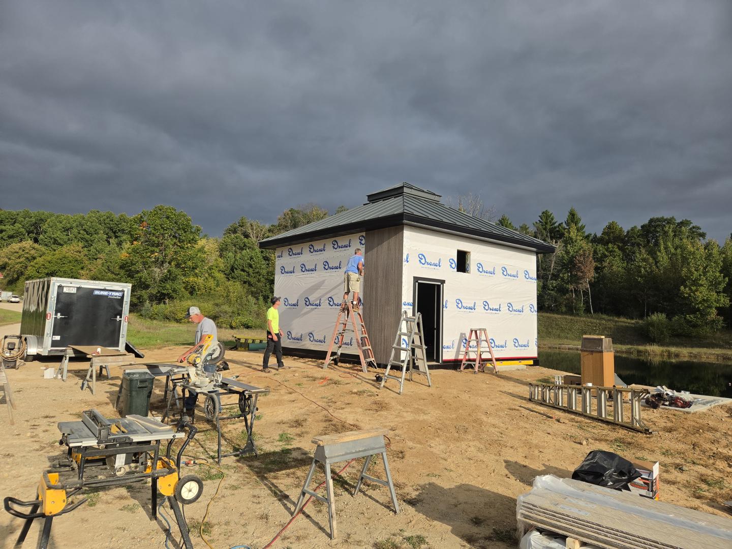 Construction site with workers building a small house under cloudy skies.