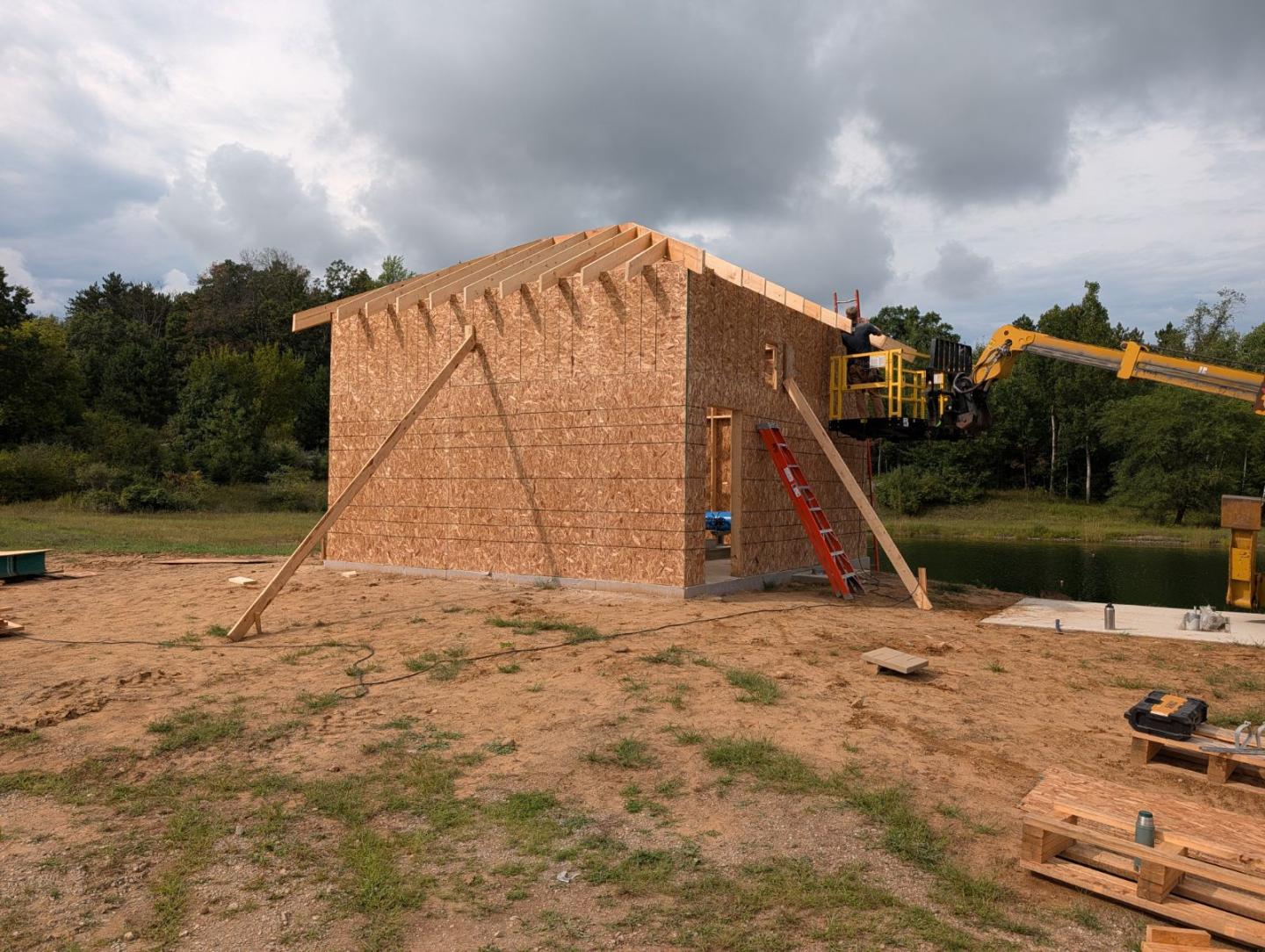 Brick building under construction beside a pond, with ladders and cloudy sky