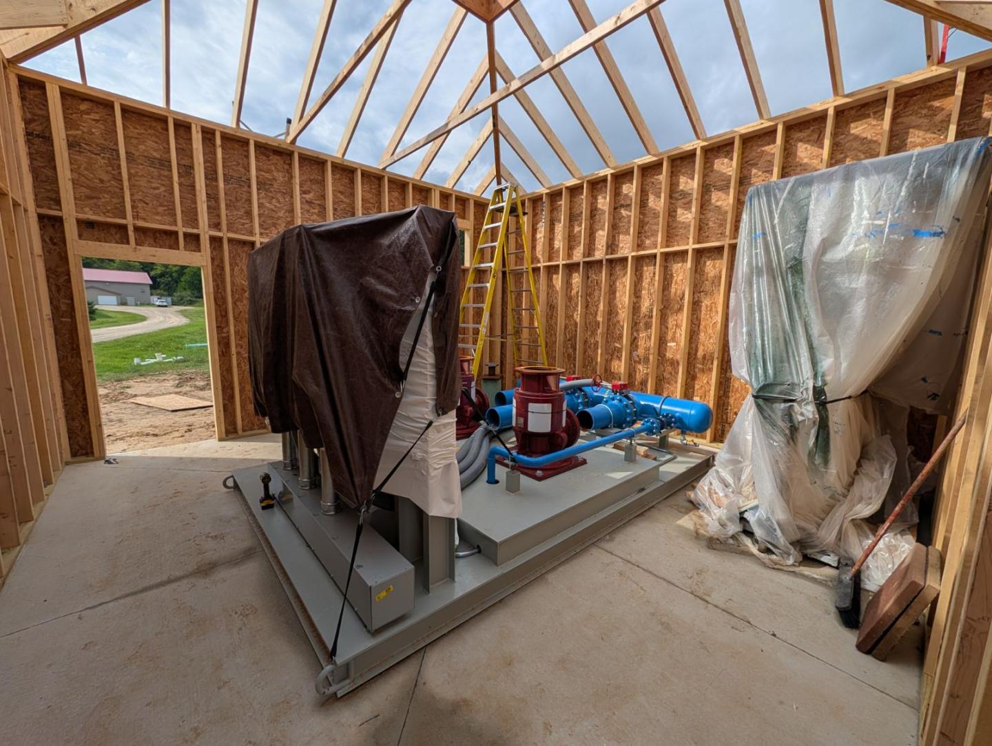 Wood-framed construction interior with covered equipment and exposed roof trusses.