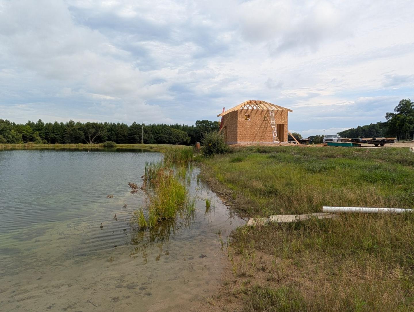 Brick building beside a calm lake with grassy shoreline under cloudy sky