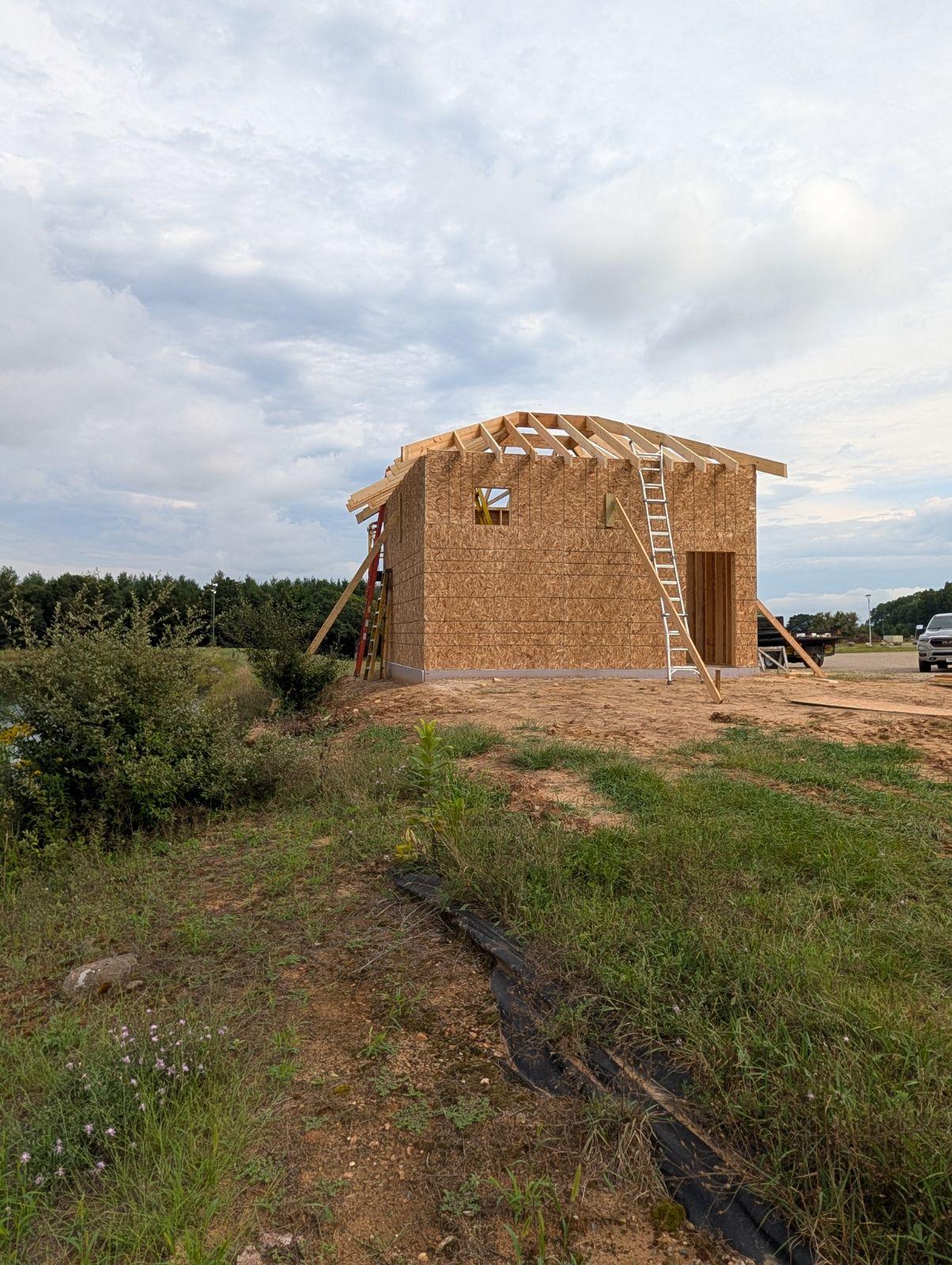 Small wooden house under construction in a grassy rural field.