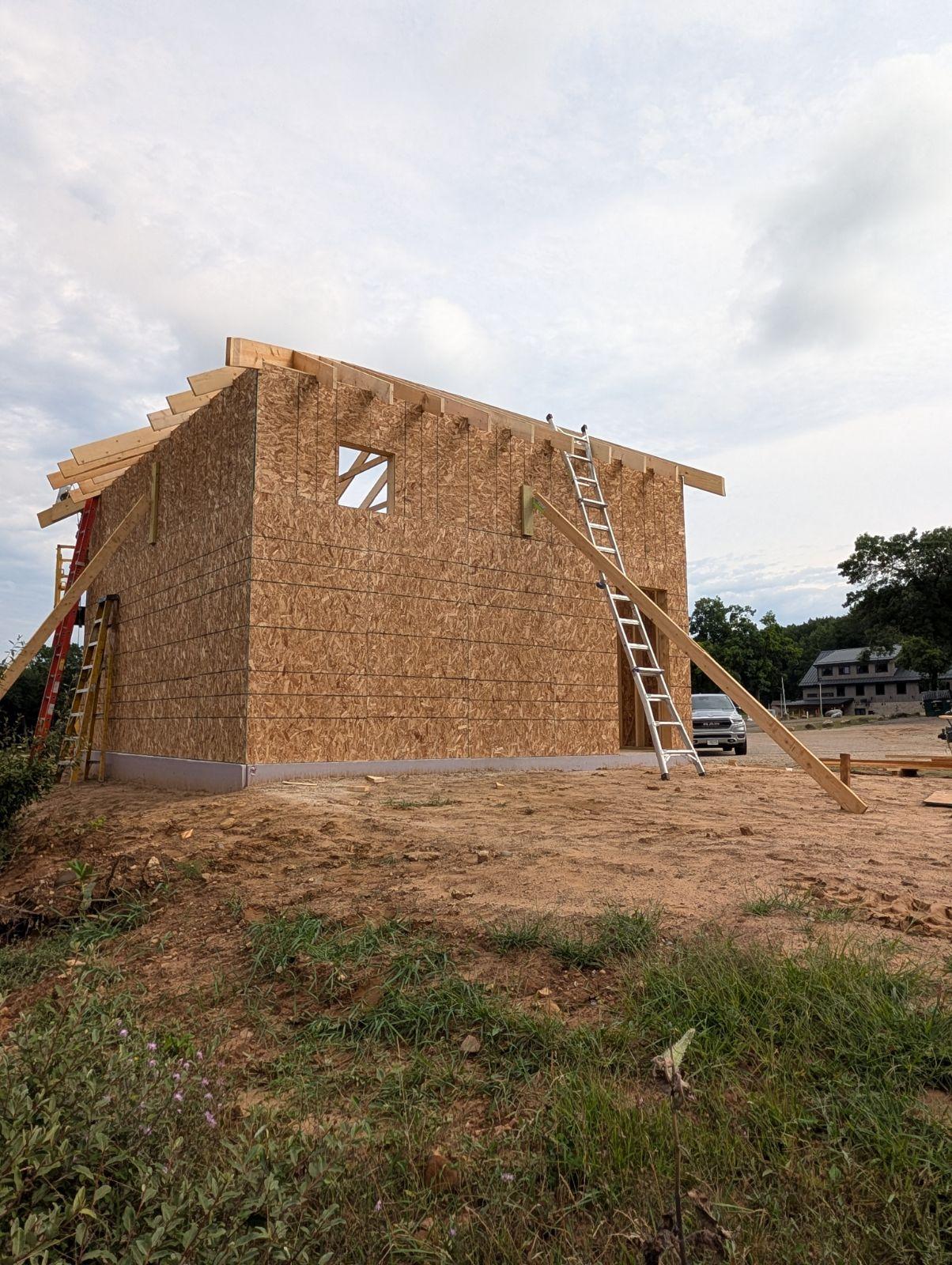 Partially built wooden house frame with ladders under a cloudy sky