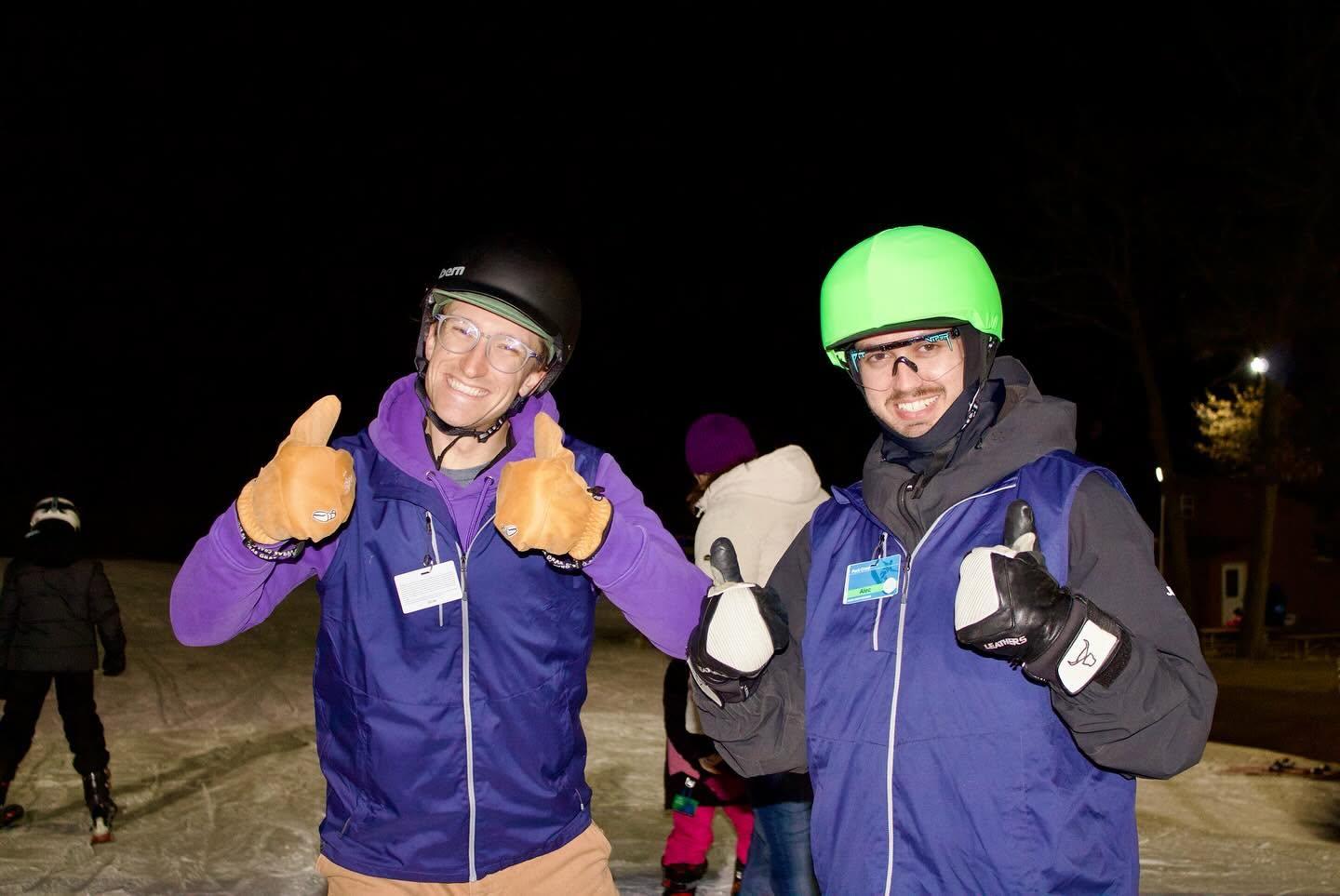 Two bundled-up men giving thumbs-up outdoors at night.