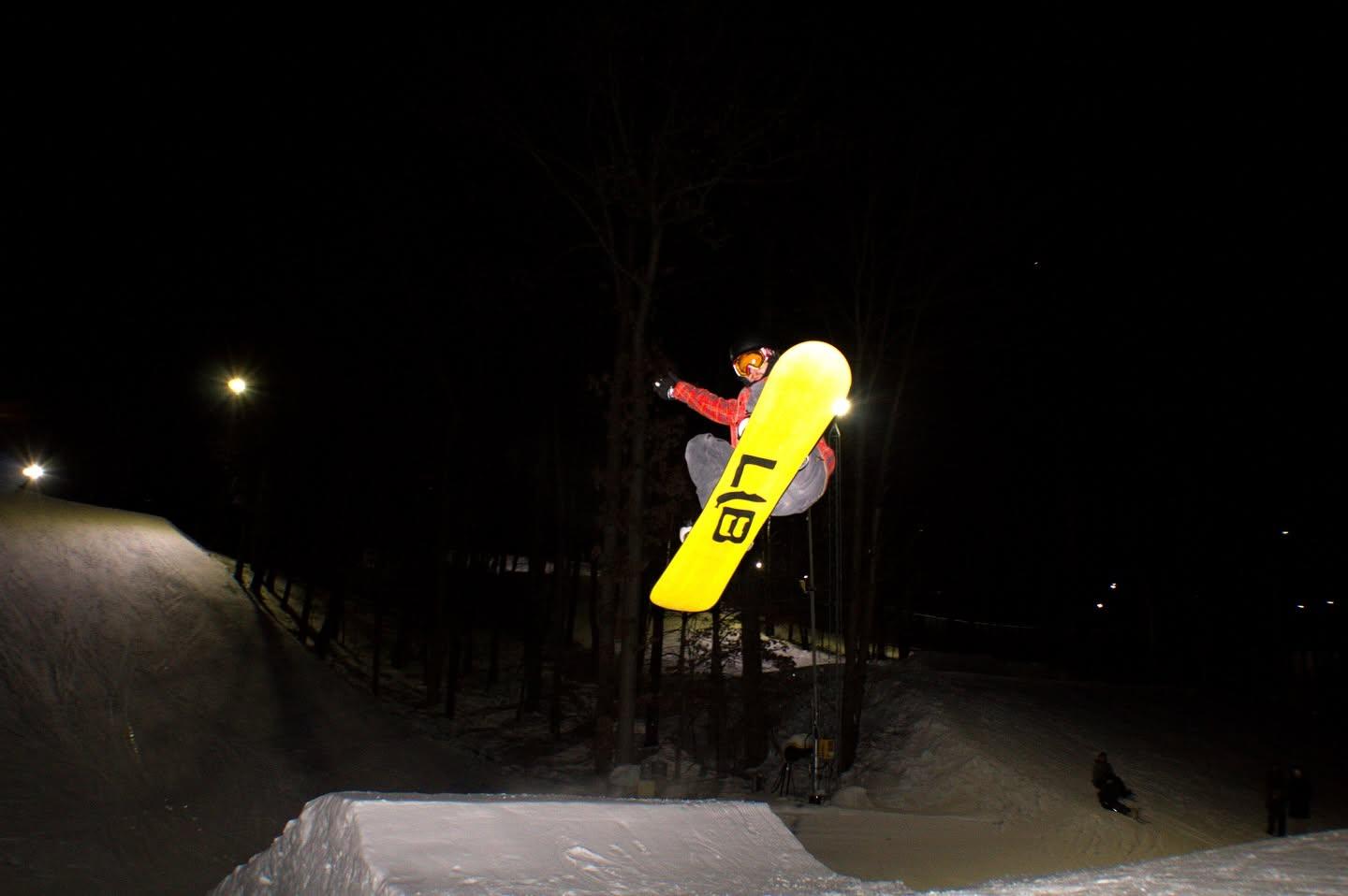 Snowboarder performing a jump at night under bright lights.
