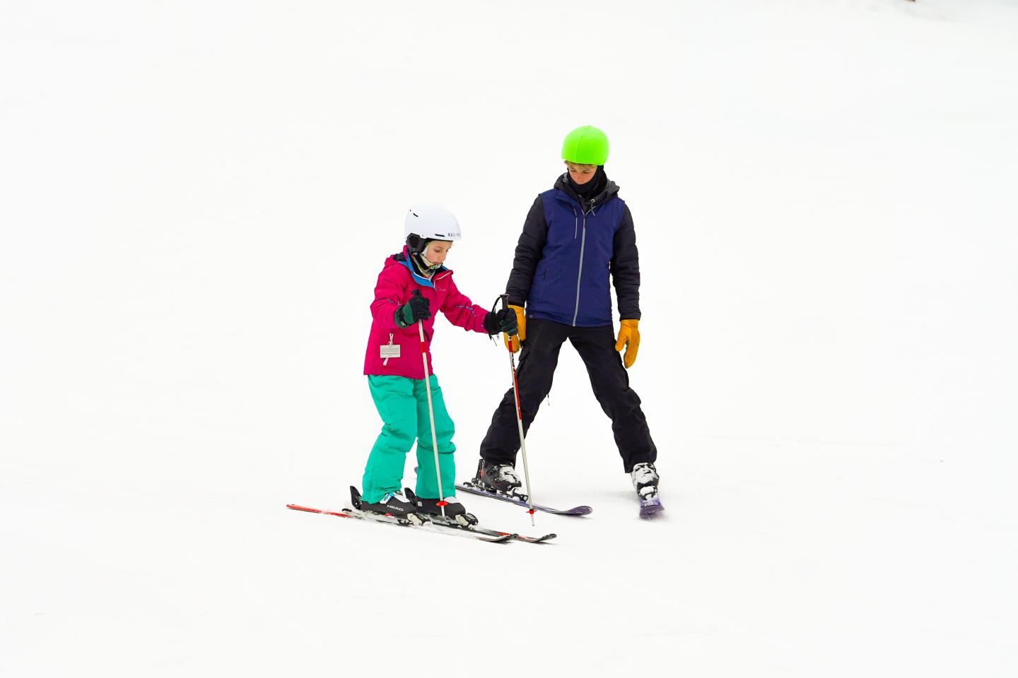Adult helping a child ski on a snowy slope.