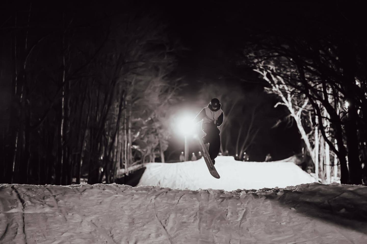 Skier silhouetted against a bright light on a snowy night slope.