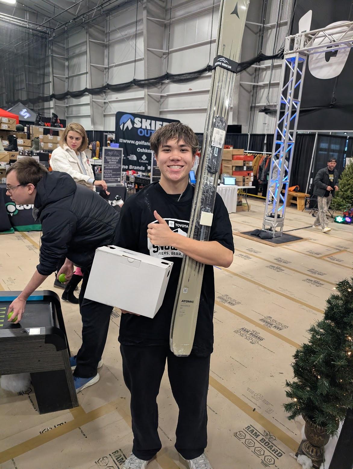Smiling young man in black shirt and apron standing in a busy hardware store.