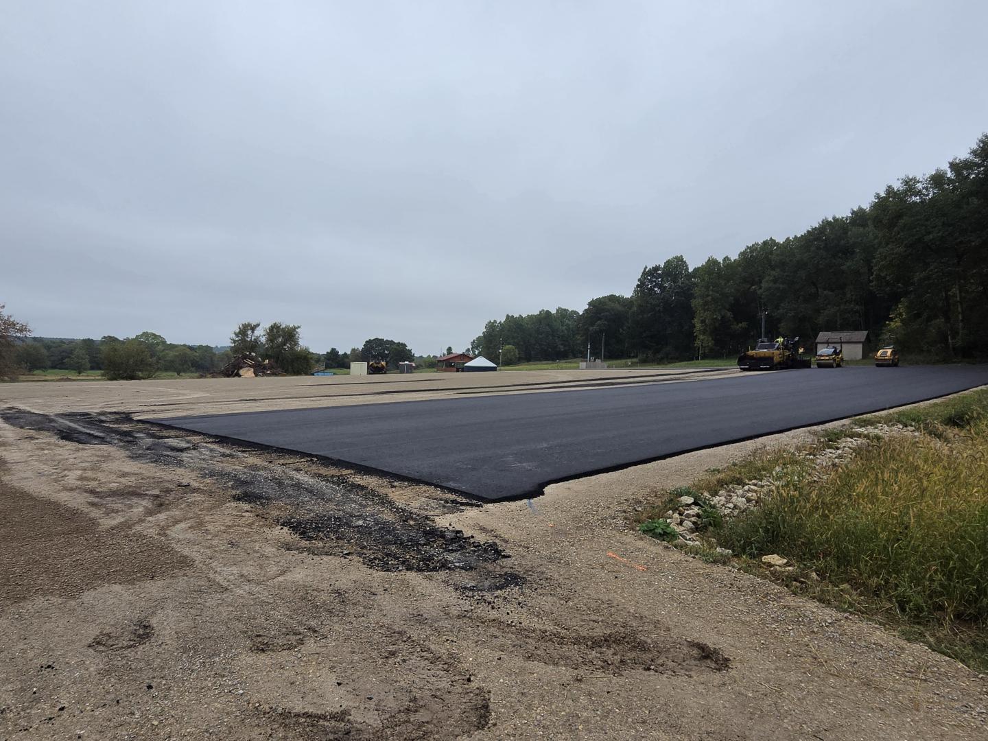 Fresh black asphalt paving on a rural road under a cloudy sky.