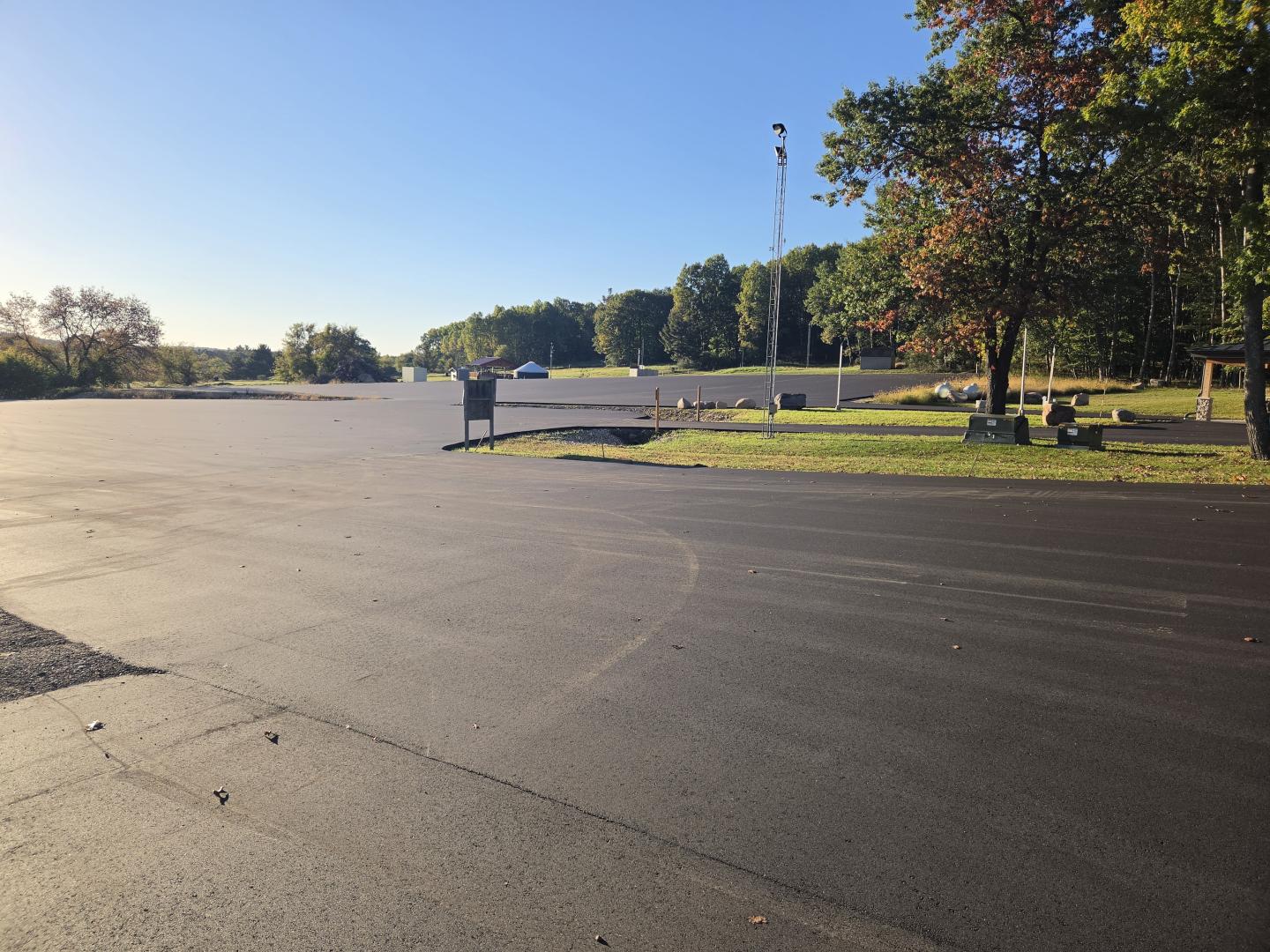 Sunlit empty schoolyard with basketball hoops and trees in the background.